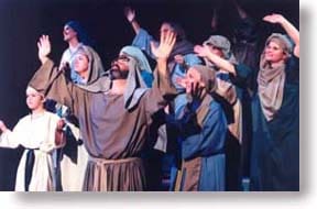 A group of adults and children in Bible costumes with their hands lifted in worship.